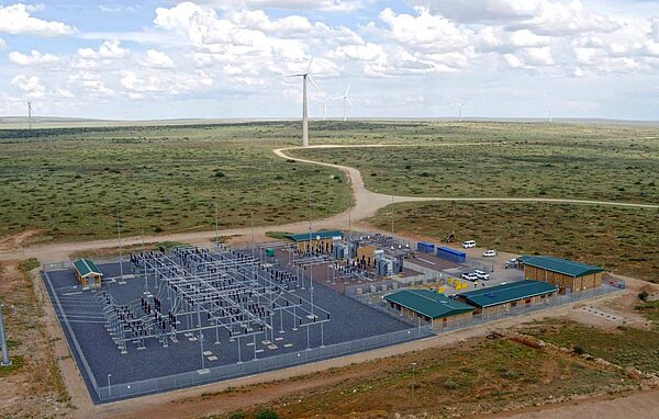 A large substation stands directly in front of a wind energy plant.