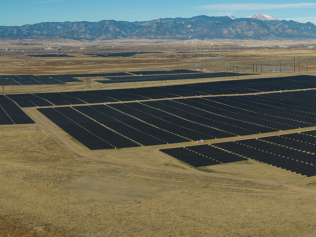 Photo of the Pike Solar Park in Colorado. Behind the massive solar park, majestic mountains rise into the blue sky.